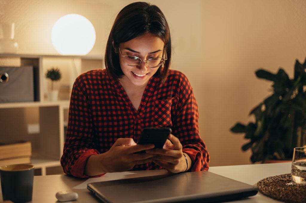 Someone at home in the evening with a laptop open and a phone in hand